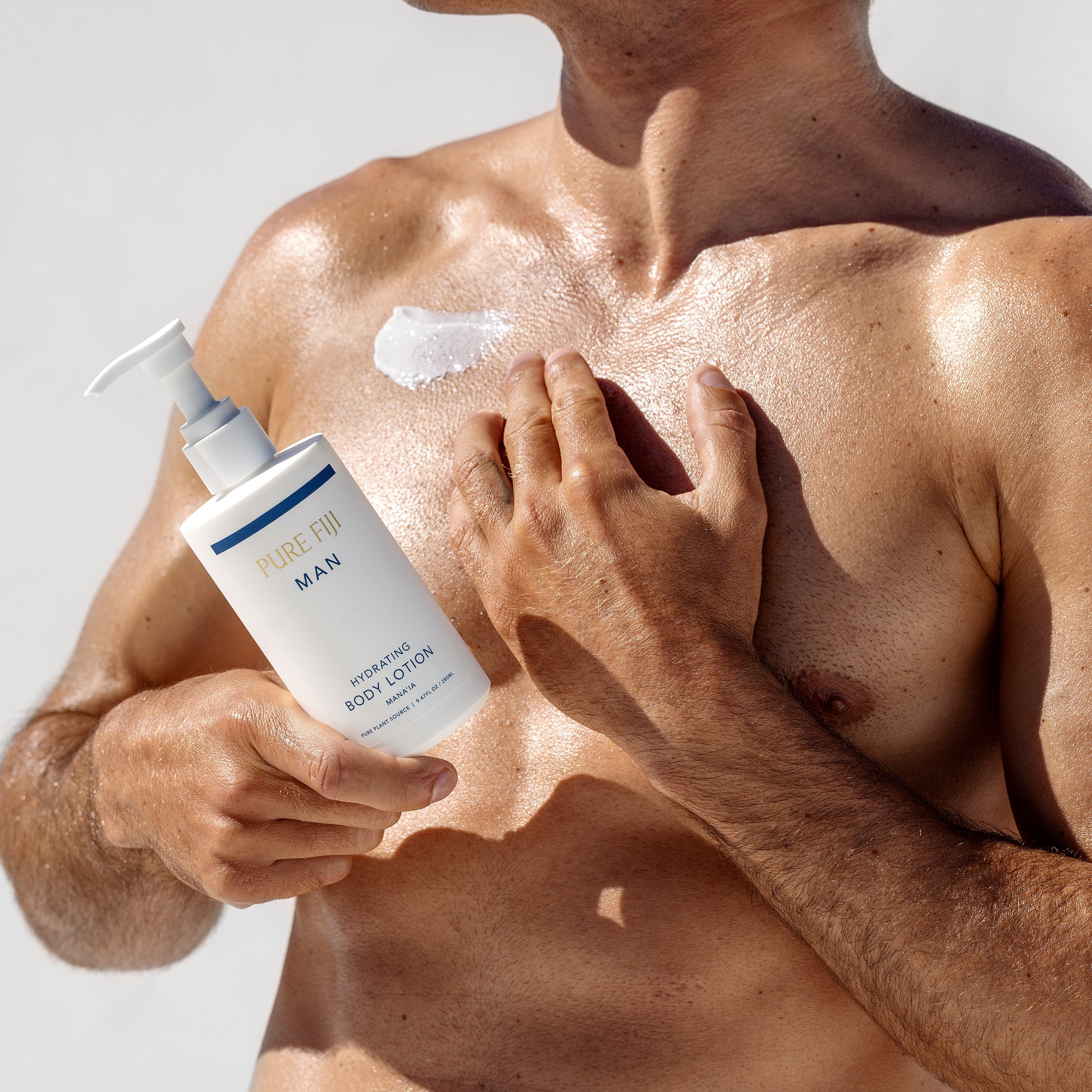 Man applying body lotion to his arm with a bottle of Pure Fiji Man Body Lotion.