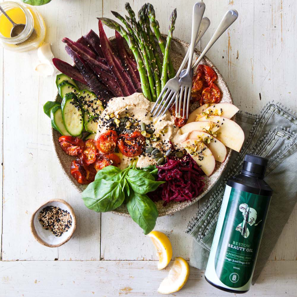 Platter of assorted vegetables with a bottle of Bestow Beauty oil on a wooden surface