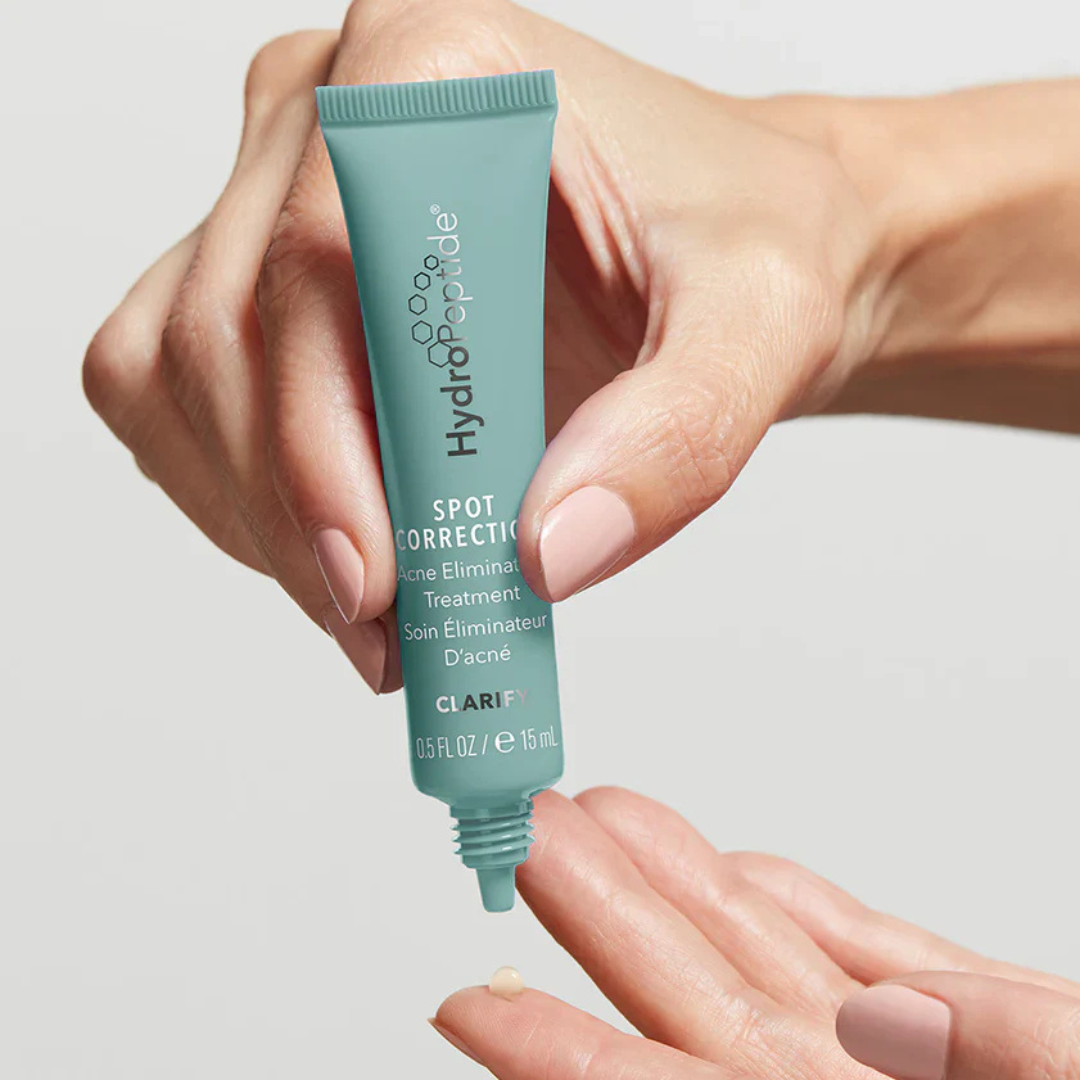 Hand holding a tube of Hydropeptide Spot Correction treatment against a neutral background