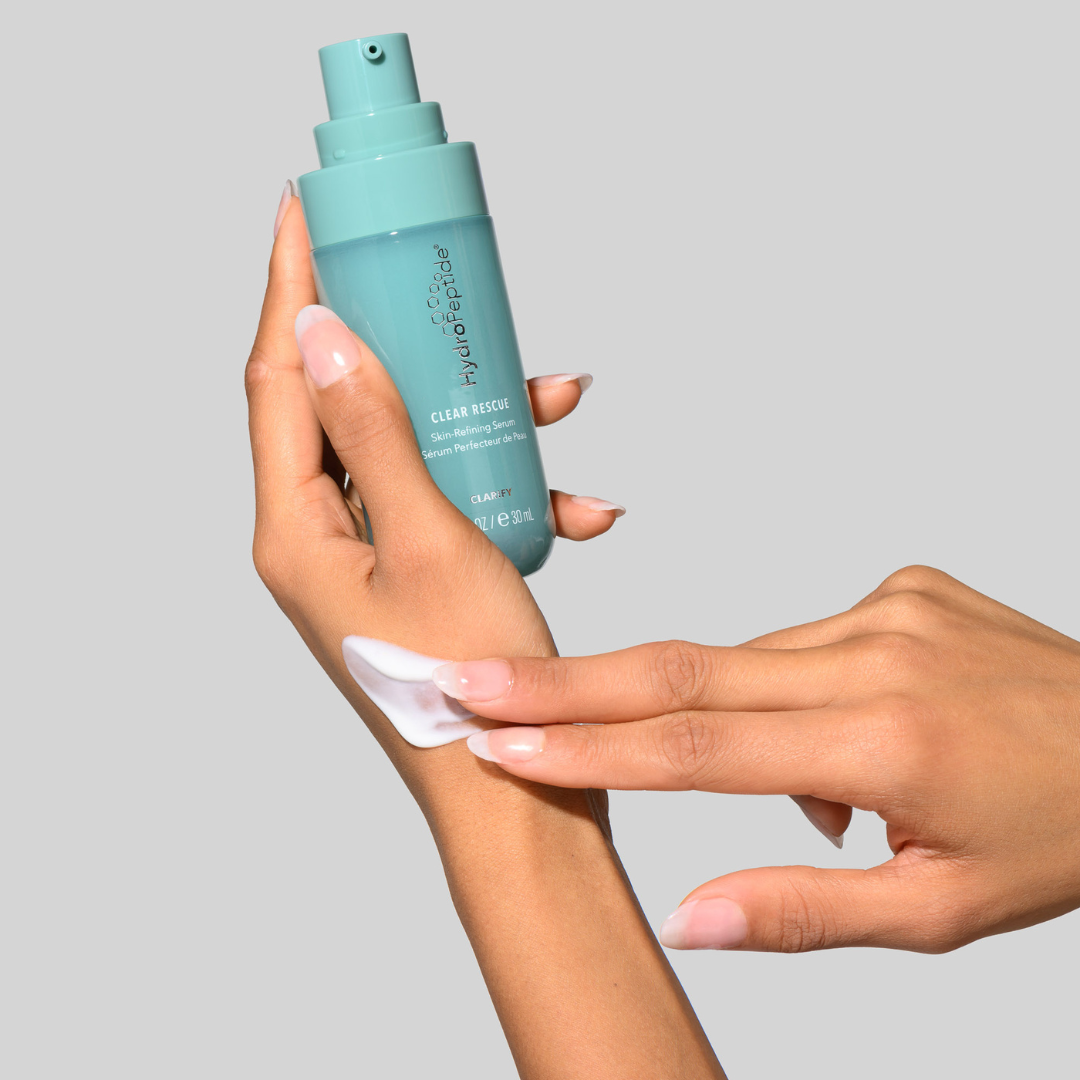 Hand holding a blue bottle of Clear Rescue Serum with a gray background