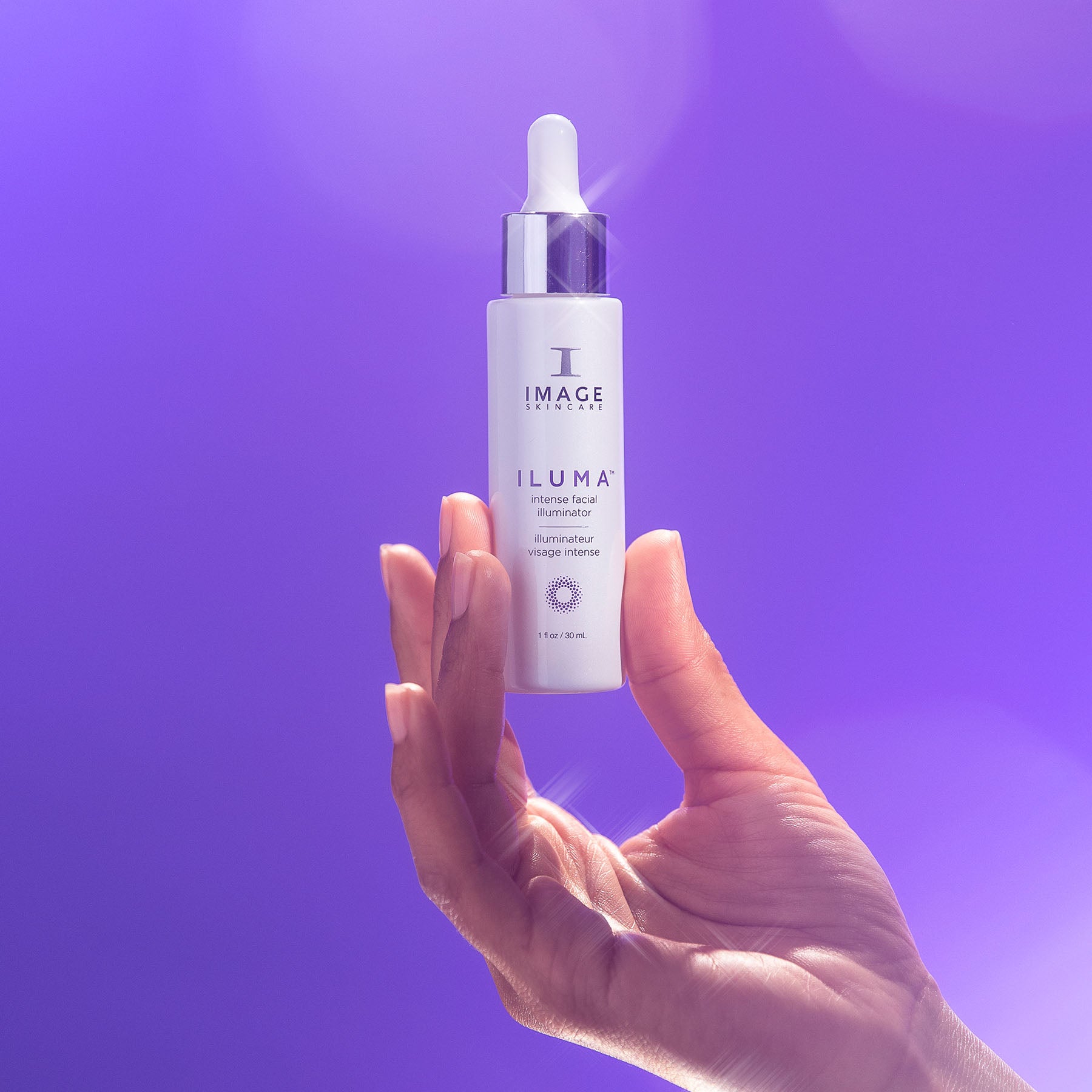 Hand holding a bottle of Image Skincare Iluma product against a purple background
