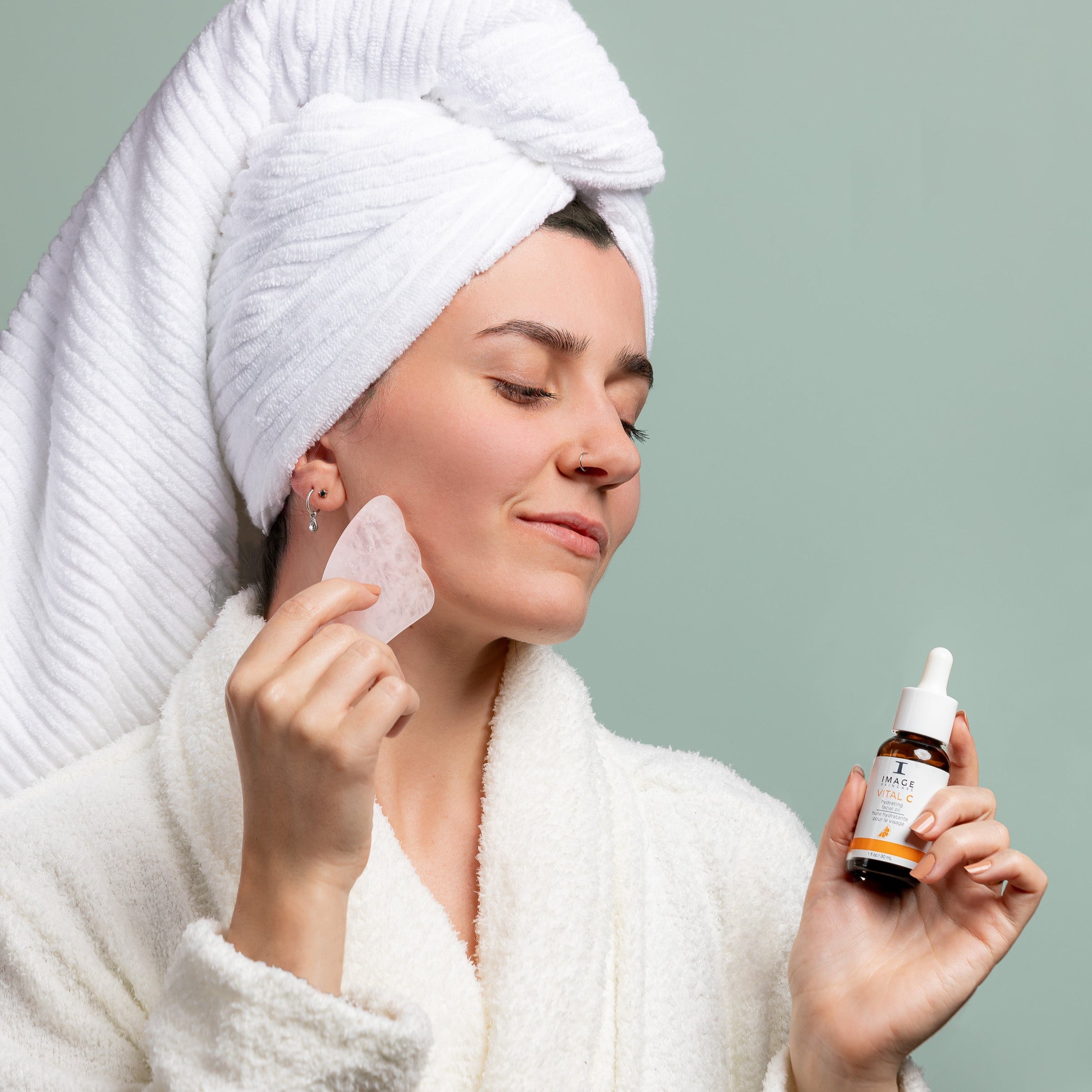 Woman applying skincare product with a dropper bottle on a plain background