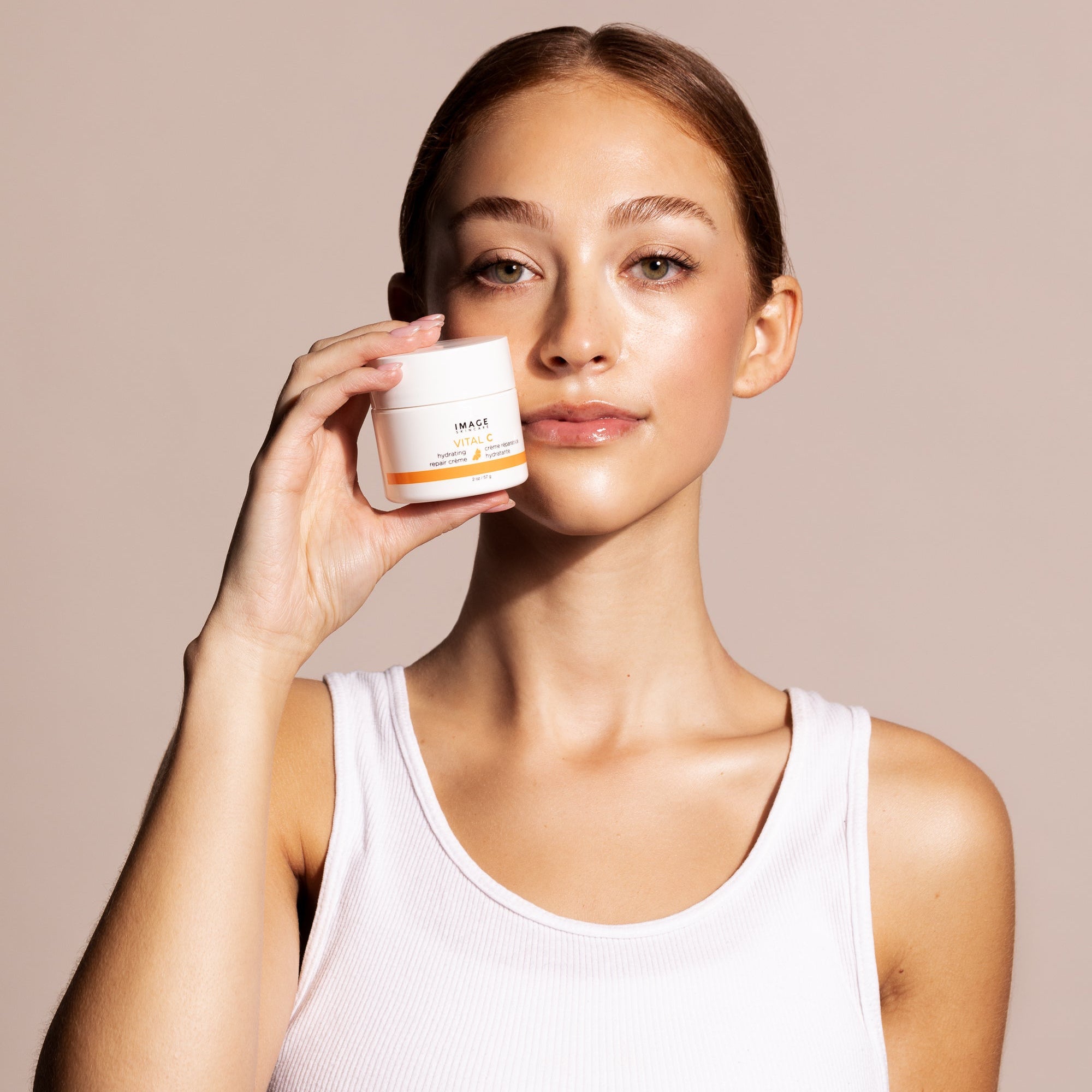 Woman holding a skincare product against a neutral background
