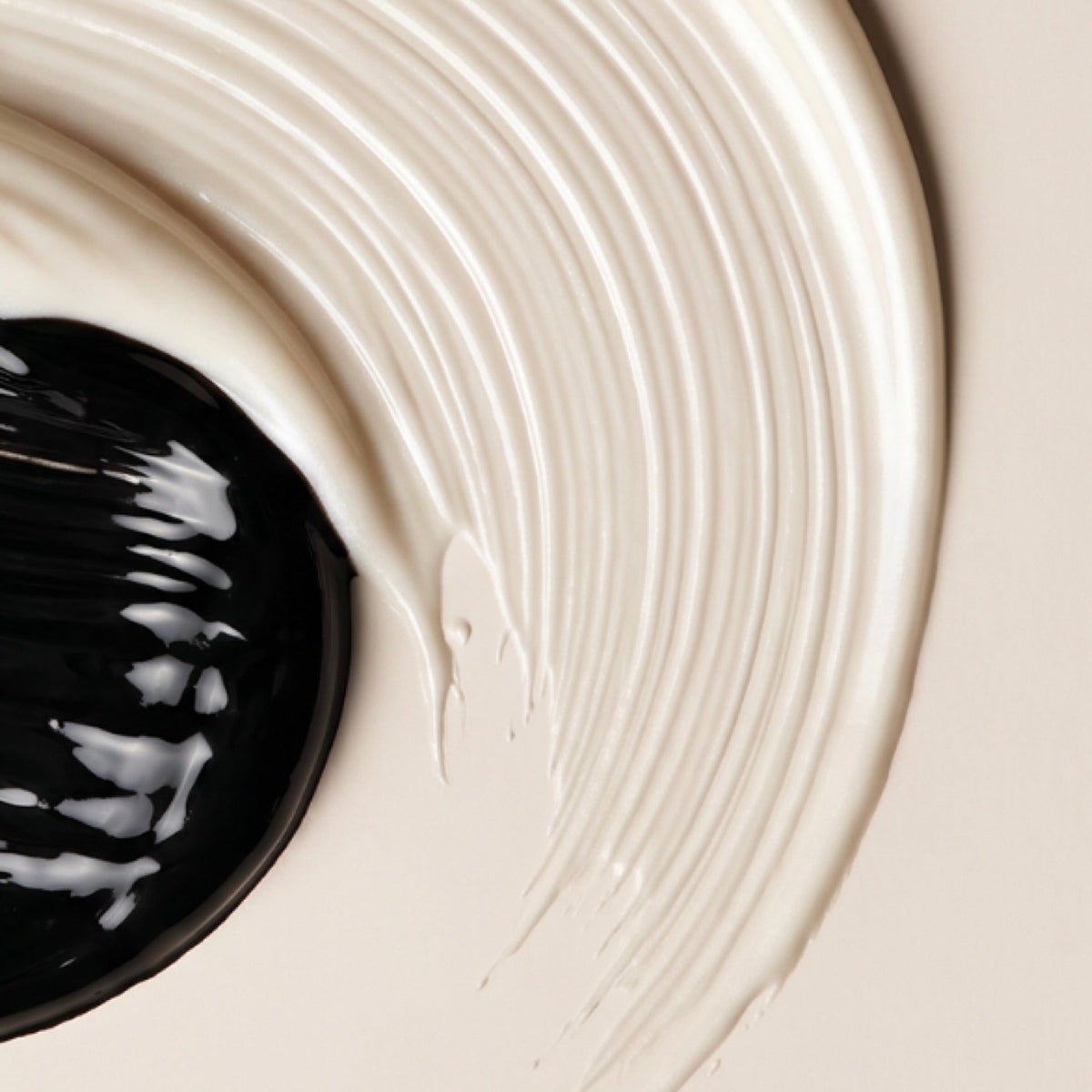A close-up of a thick cream-colored lash primer swirled in a circular motion on a light beige background, with a glossy black circular container visible in the lower left corner.