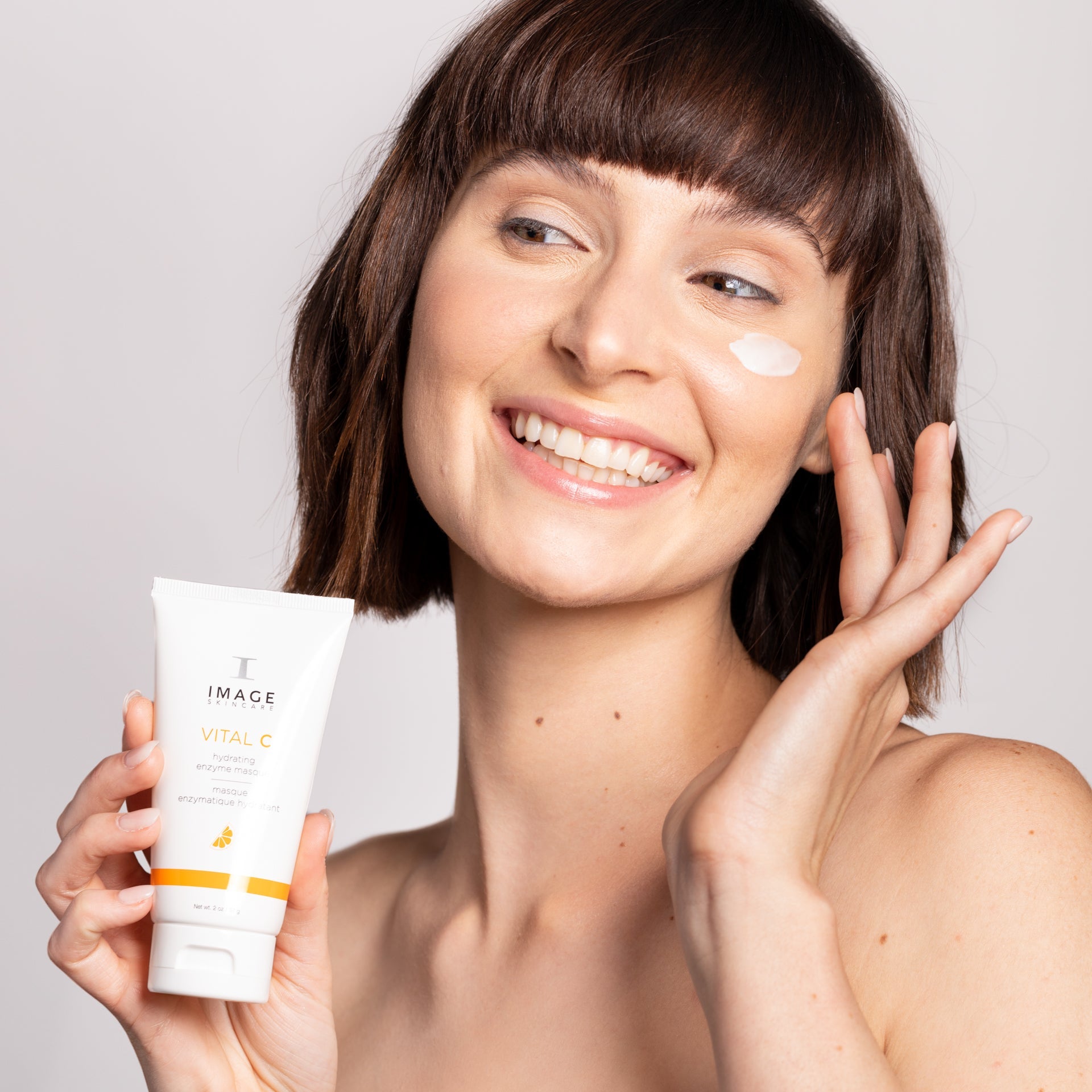 Woman applying skincare product with a tube labeled 'IMAGE' on a plain background