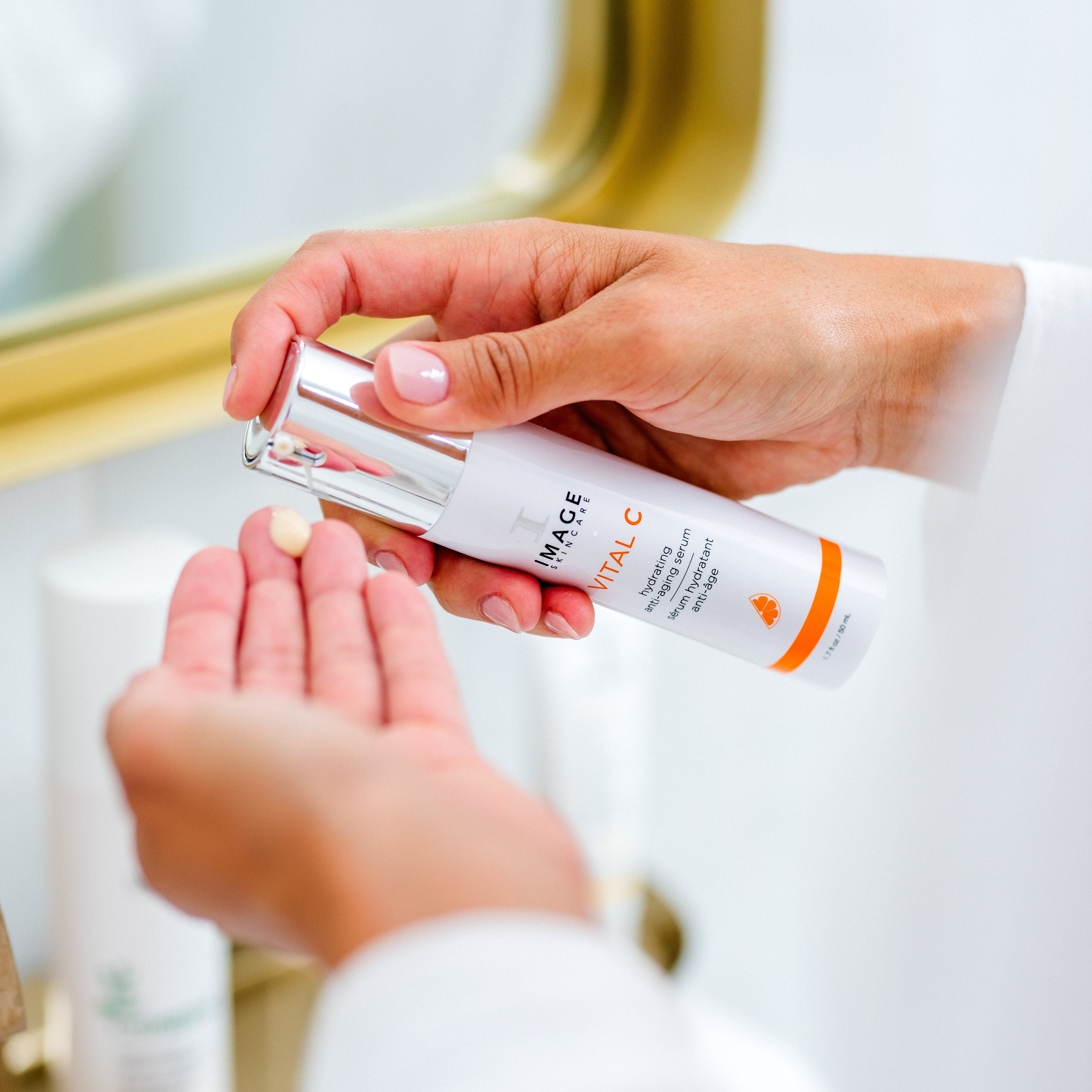 Person holding a skincare product with a mirror and other skincare bottles in the background