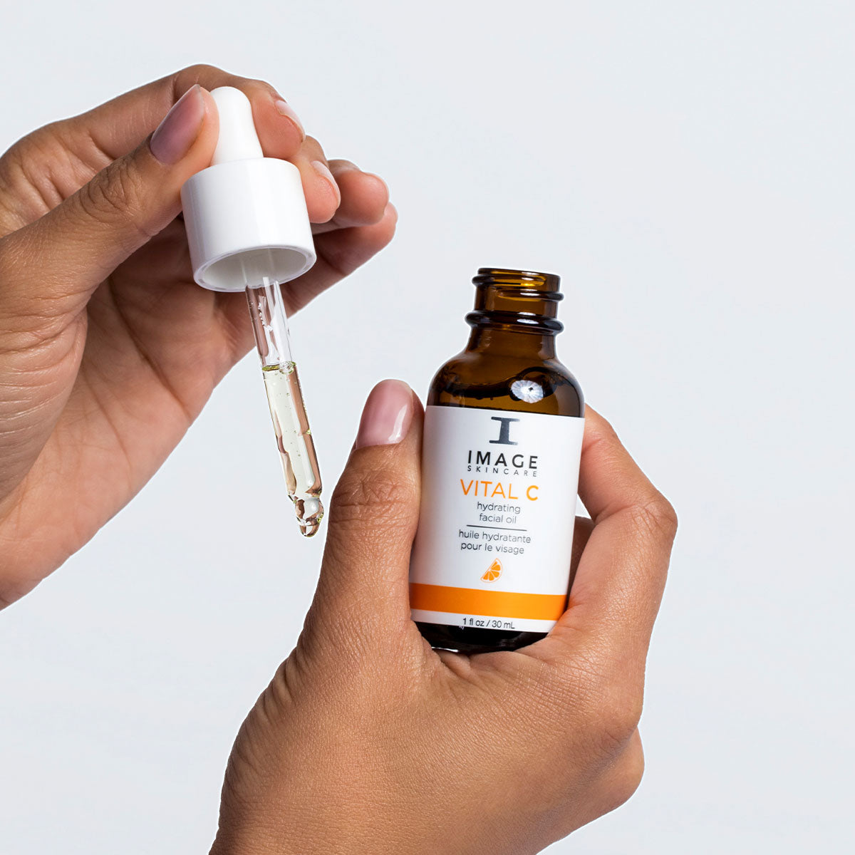 Hand holding a dropper with a bottle labeled 'IMAGE Skincare Vital C' against a light gray background