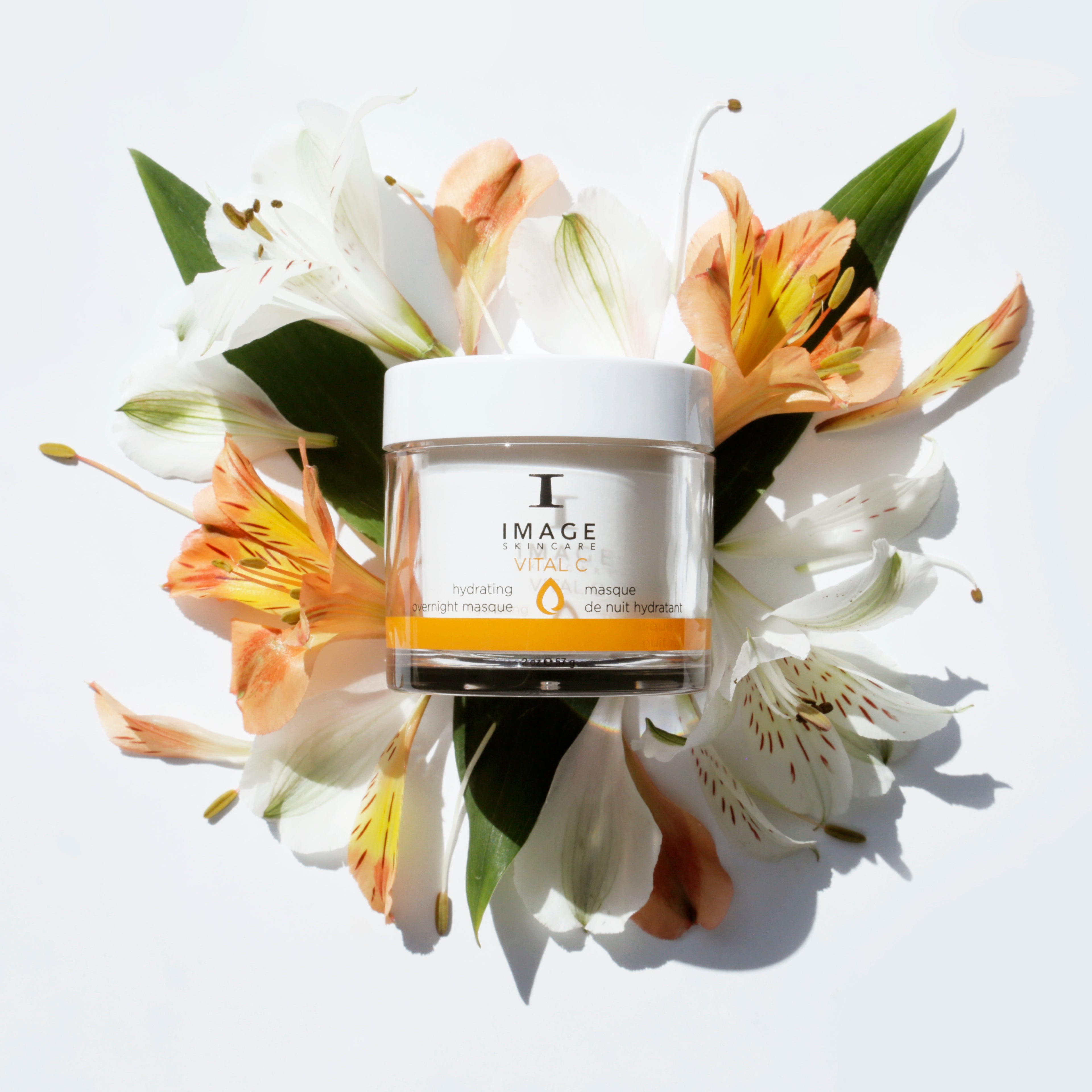 Jar of skincare product surrounded by flowers on a light background