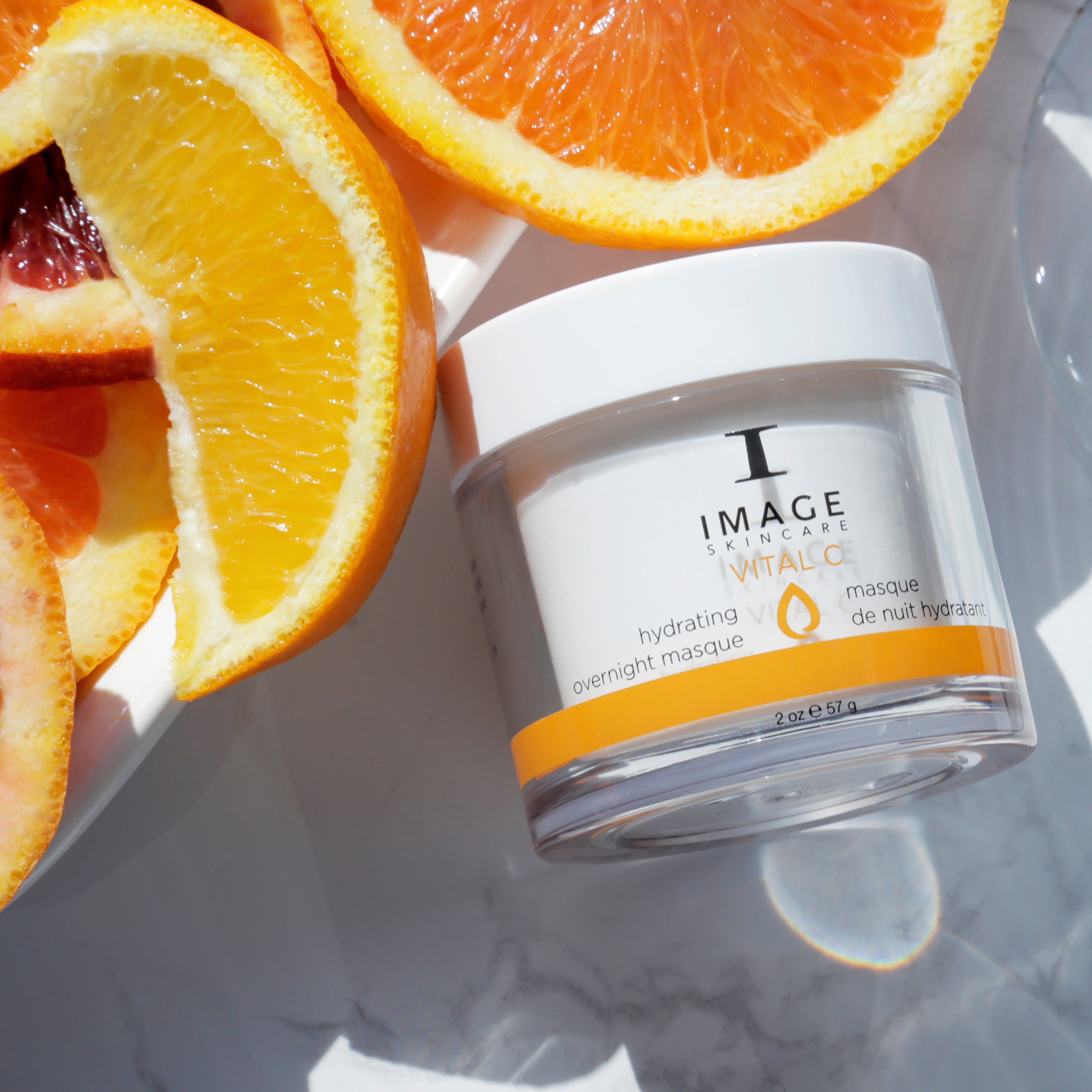 Jar of skincare product with sliced oranges on a marble surface