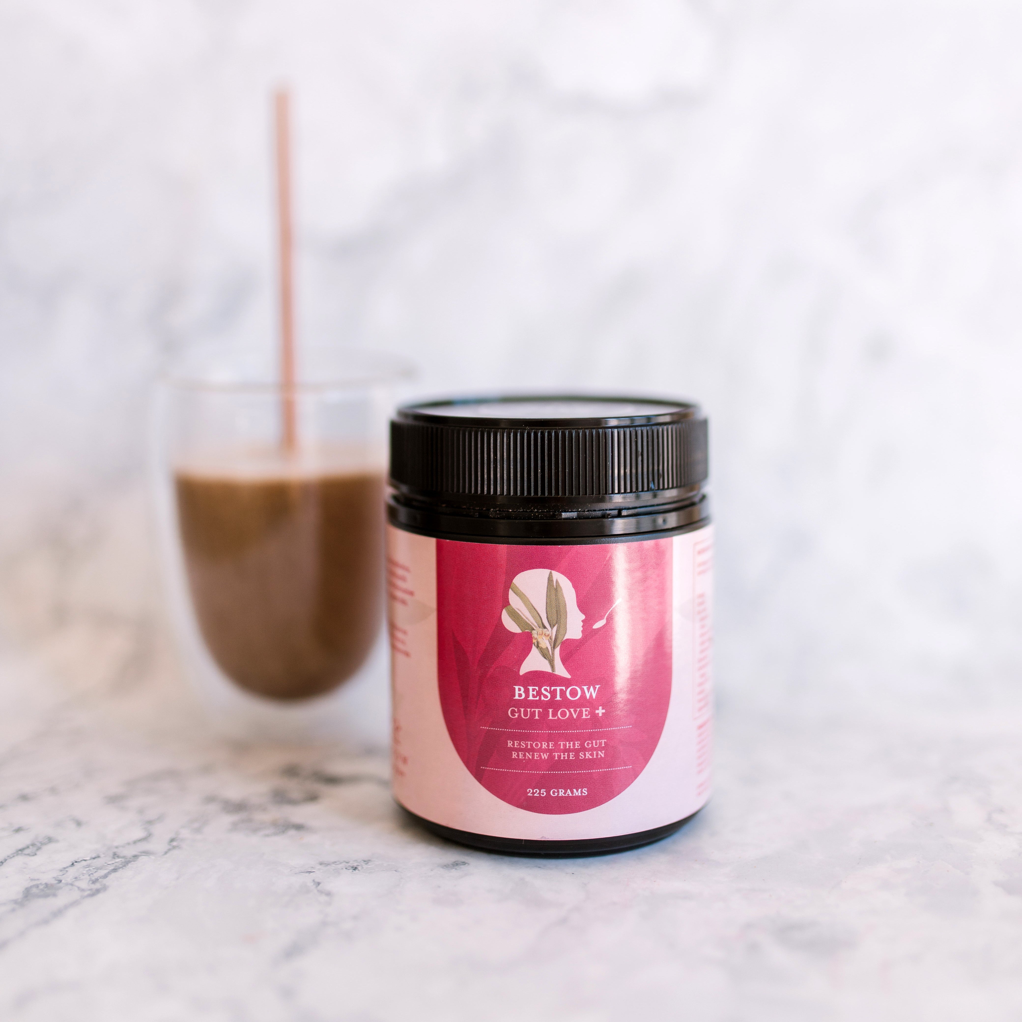 Jar of Bestow Superfood with a glass of a brown smoothie on a marble surface.