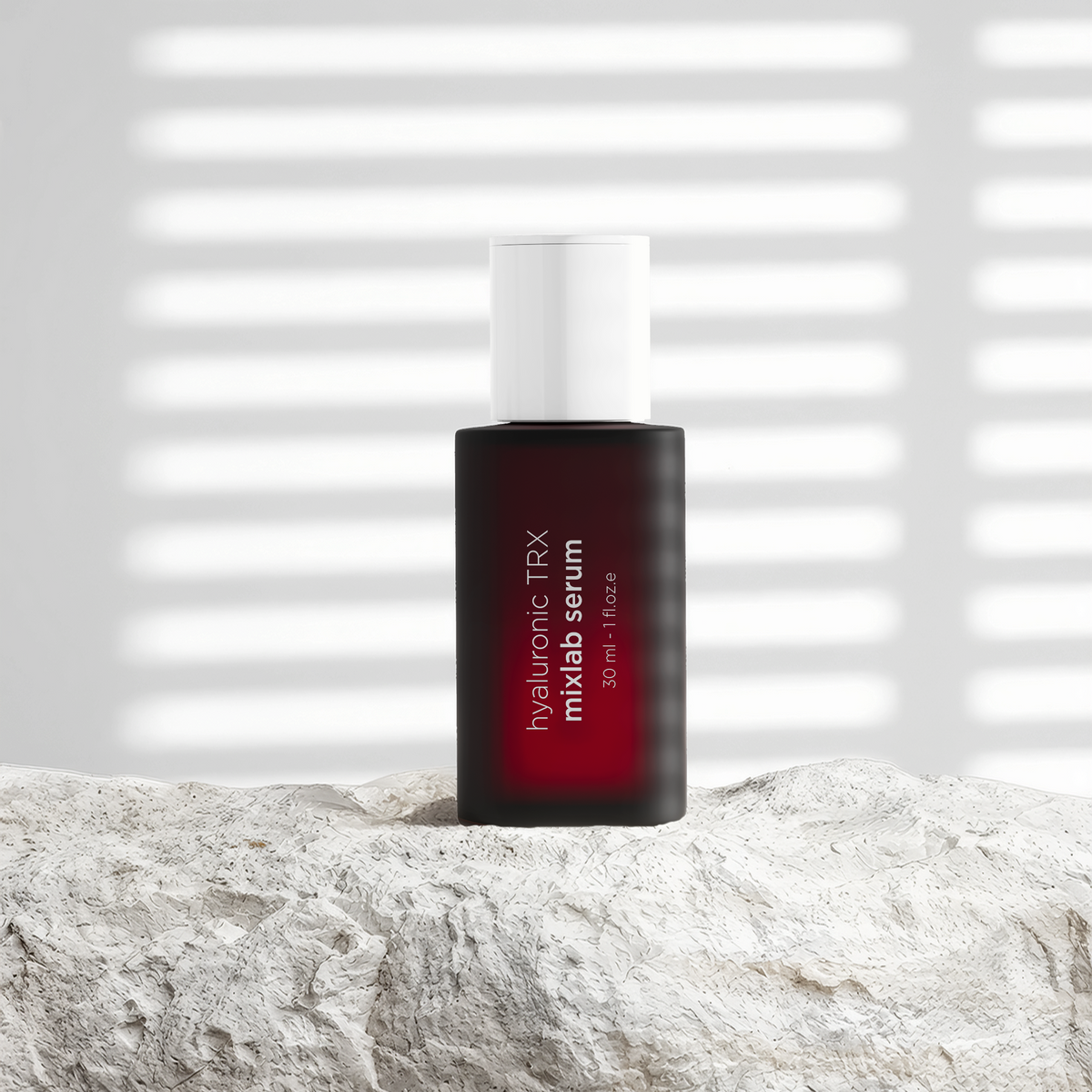 A bottle of Mixlab Serum with Hyaluronic TRX, featuring a dark red bottle and white cap, standing on a textured light gray stone surface with a background of soft horizontal window blinds.