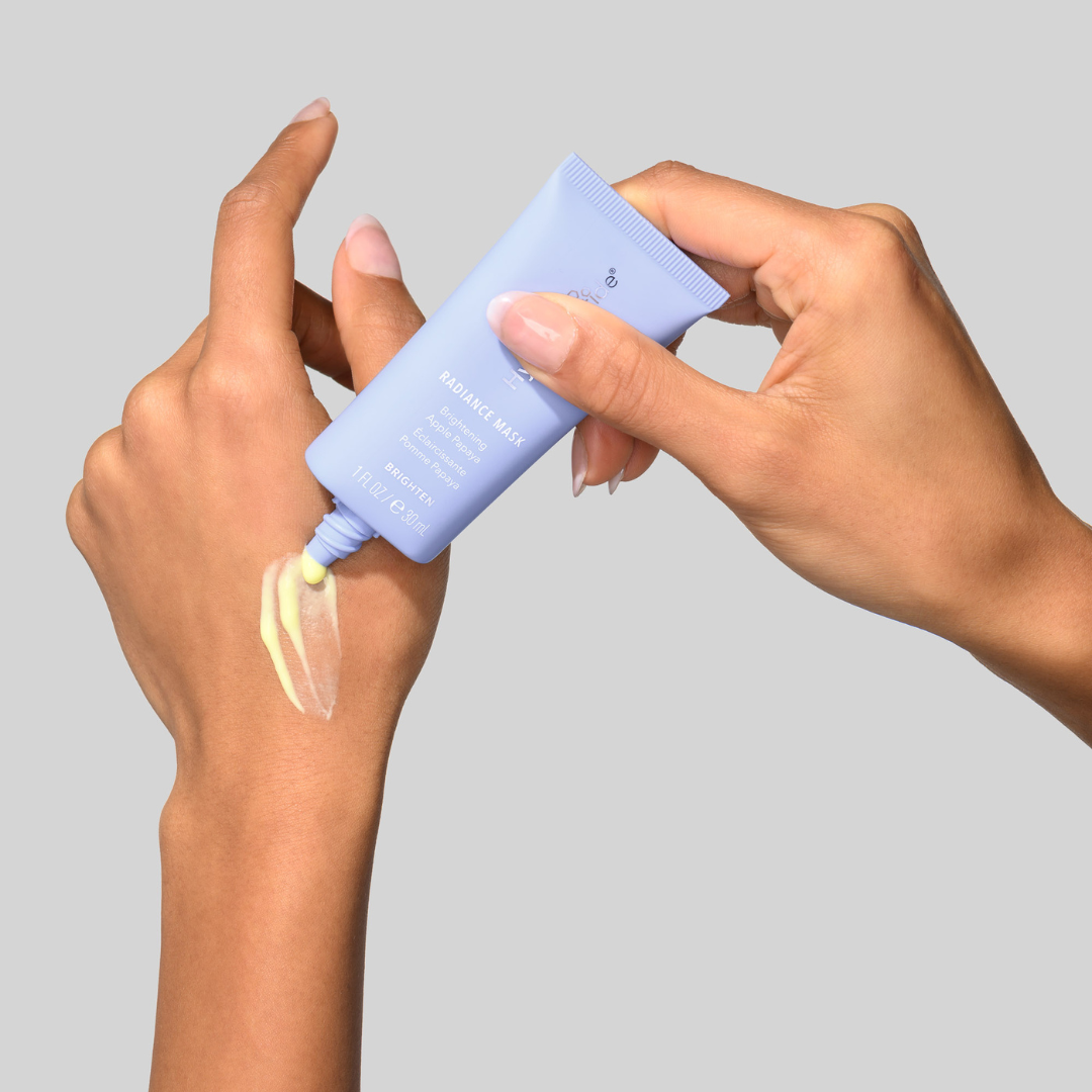 Hand applying Hydropeptide Radiance Mask from a blue tube against a gray background