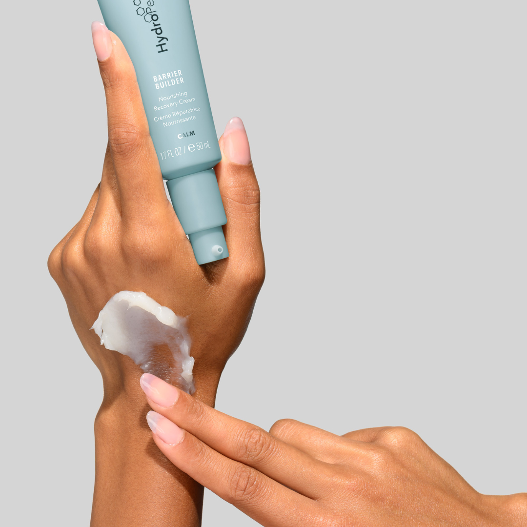 Hand applying HydroPeptide Barrier Buildert to another hand with a gray background
