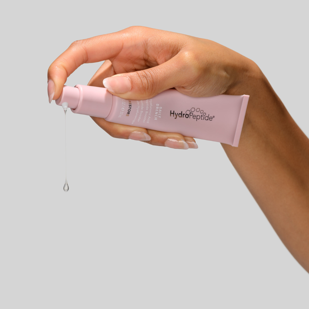Hand holding a pink HydroPeptide skincare product with a clear background
