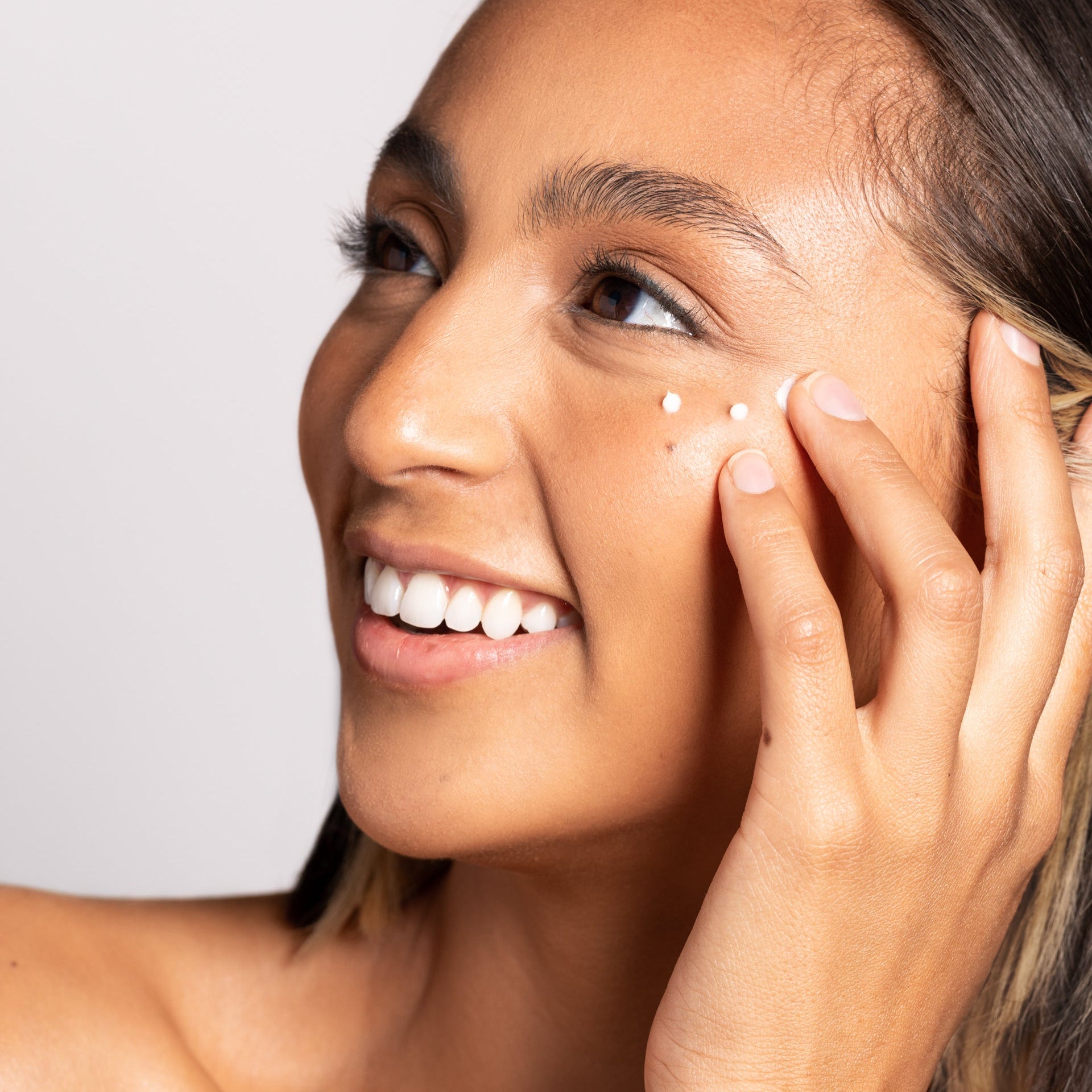 Woman applying cream to her face with a neutral background