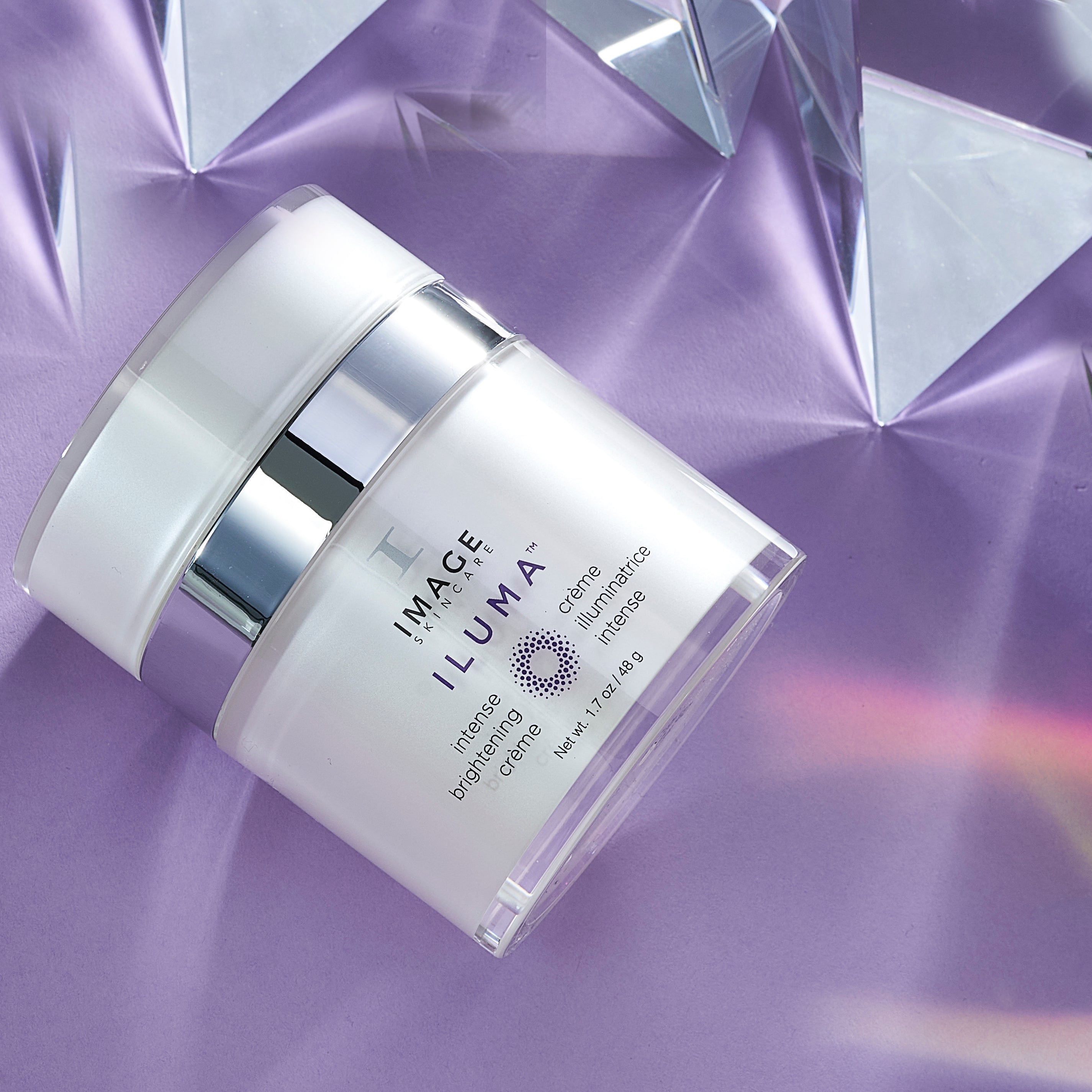 Skincare jar labeled 'IMAGE ILUMA' on a reflective purple surface with geometric shapes.