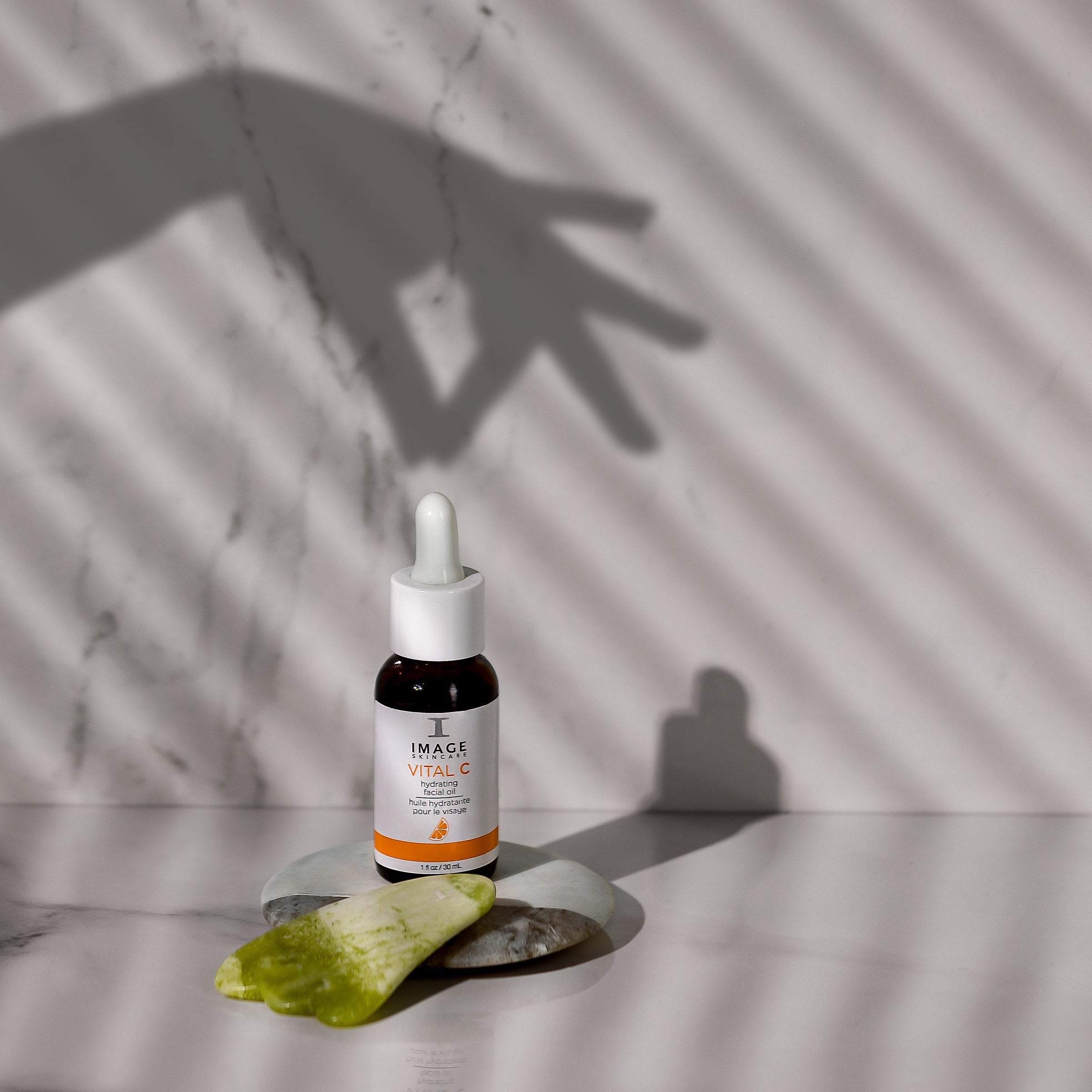 Bottle of skincare serum with dropper on a marble surface with shadows