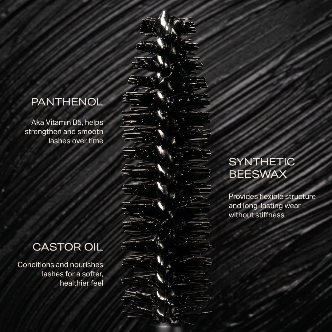 A Youngblood black eyelash brush shown upright on a dark textured background with white text describing ingredients: panthenol, synthetic beeswax, and castor oil.