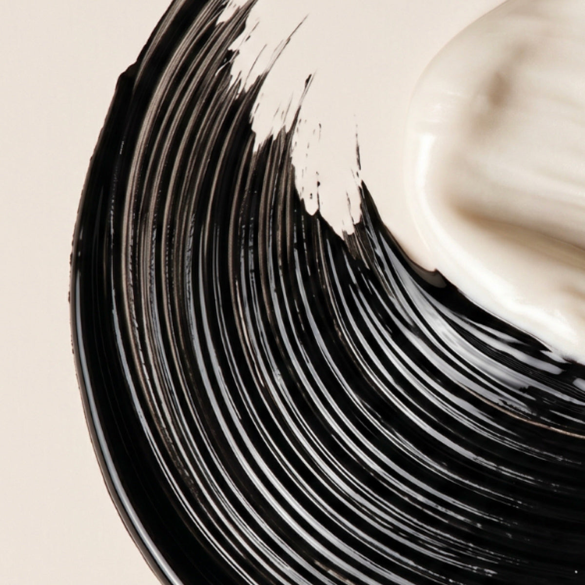 A close-up of a thick black cosmetic Mascara cream swirled on a light beige background, with part of a white cream visible at the top right.