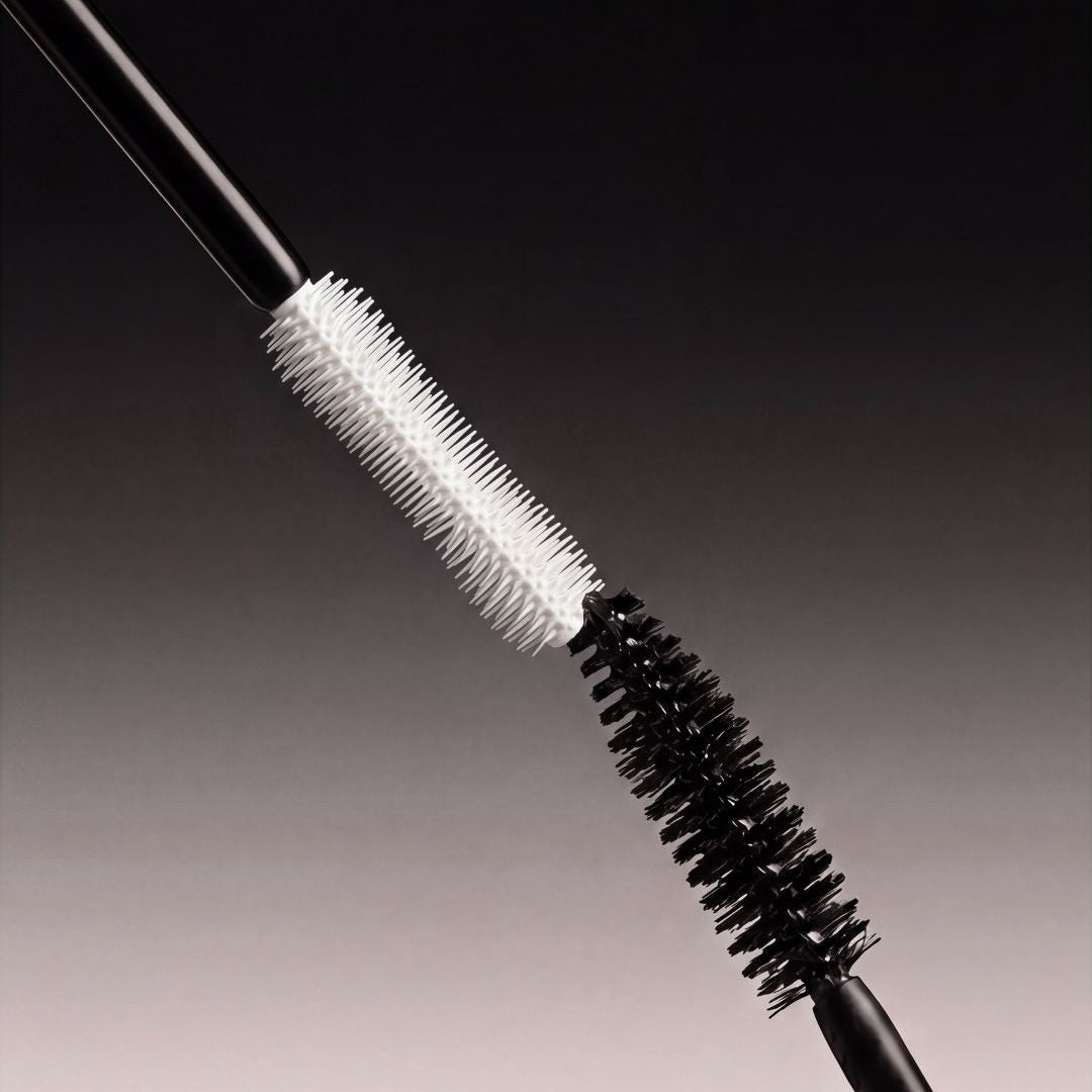 Two black cosmetic mascara wands with lash primer and mascara shown diagonally against a dark-to-light gray gradient background.