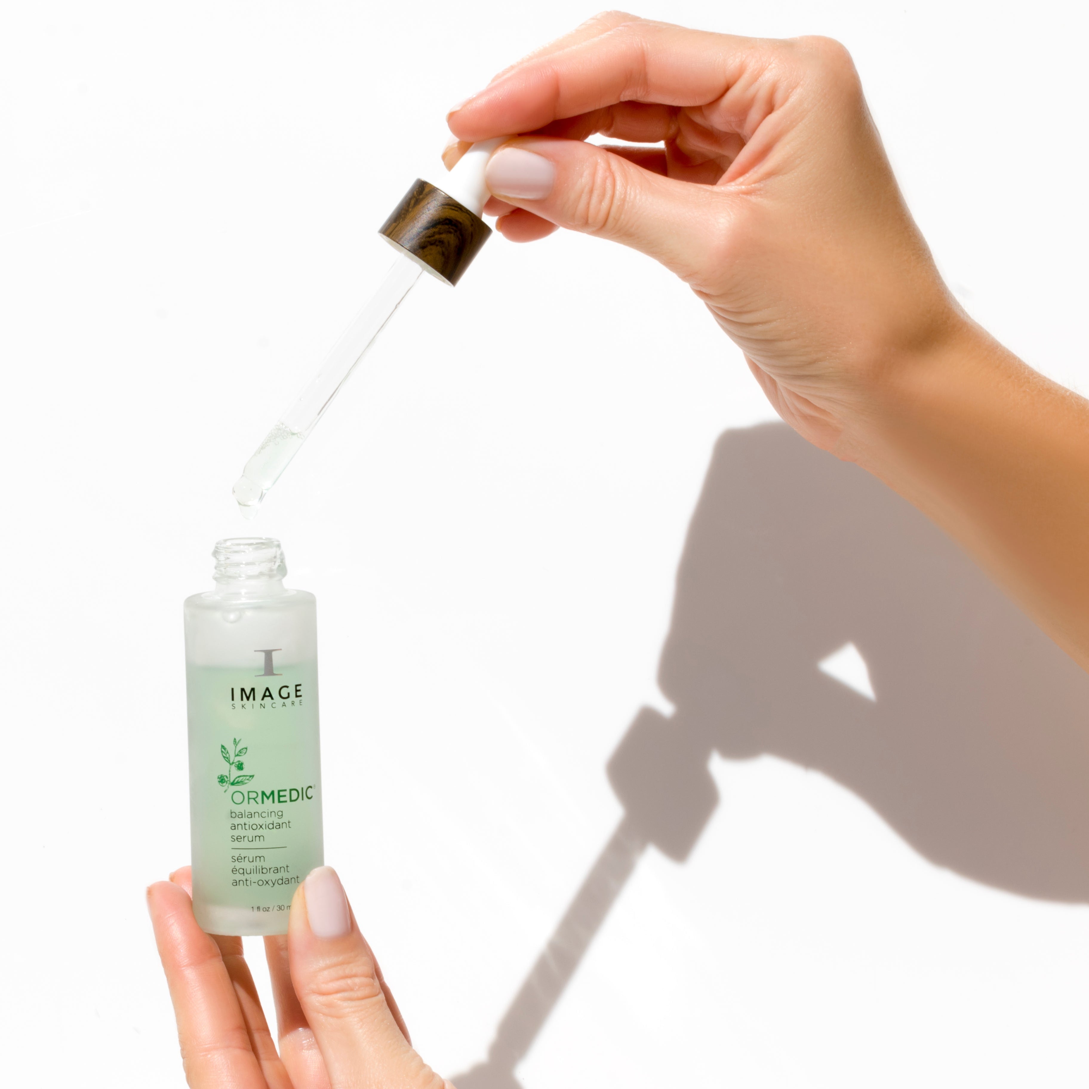 Hand holding a dropper over a skincare serum bottle with a white background
