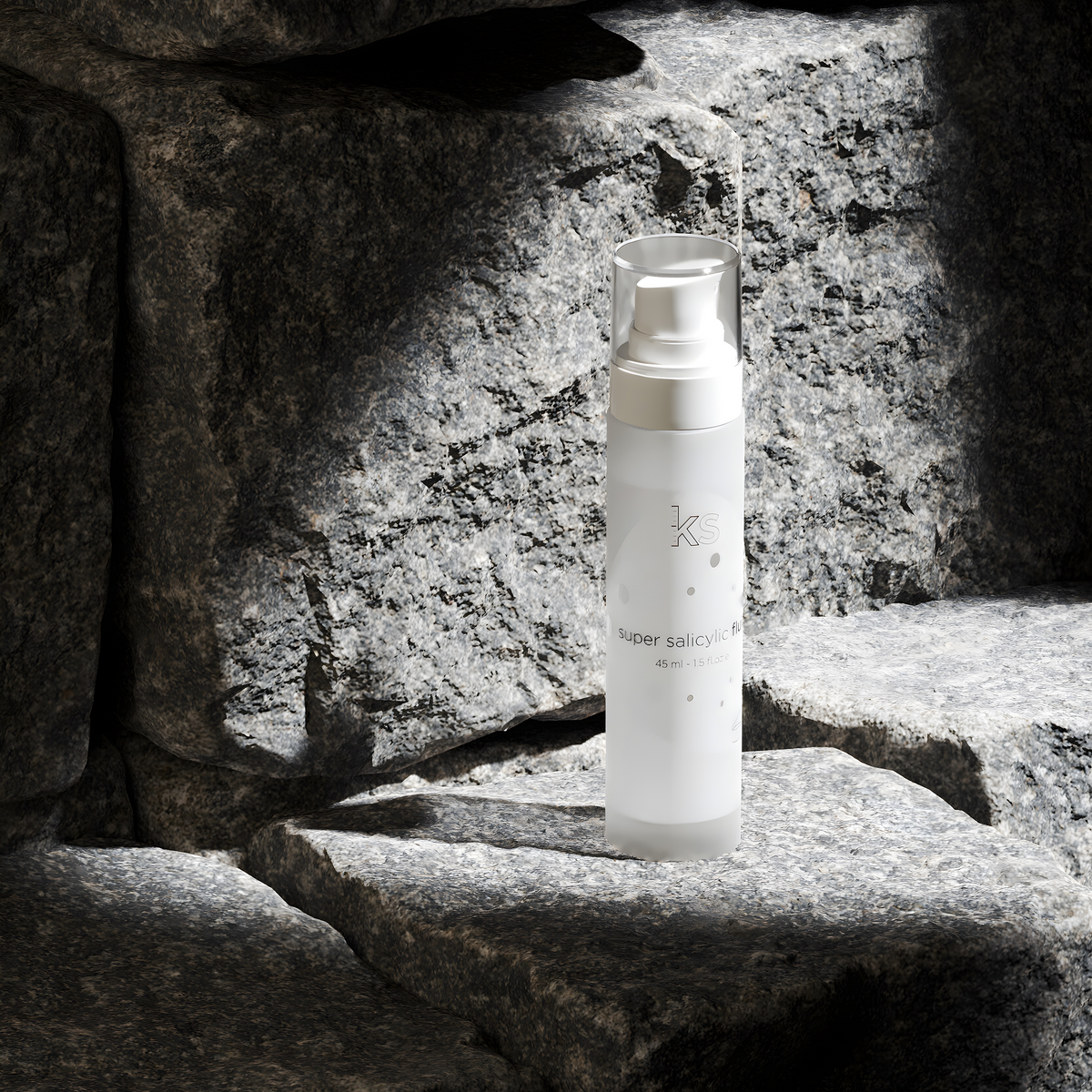 A frosted glass skincare pump bottle with a clear cap stands on dark stone steps in dramatic, high-contrast lighting.