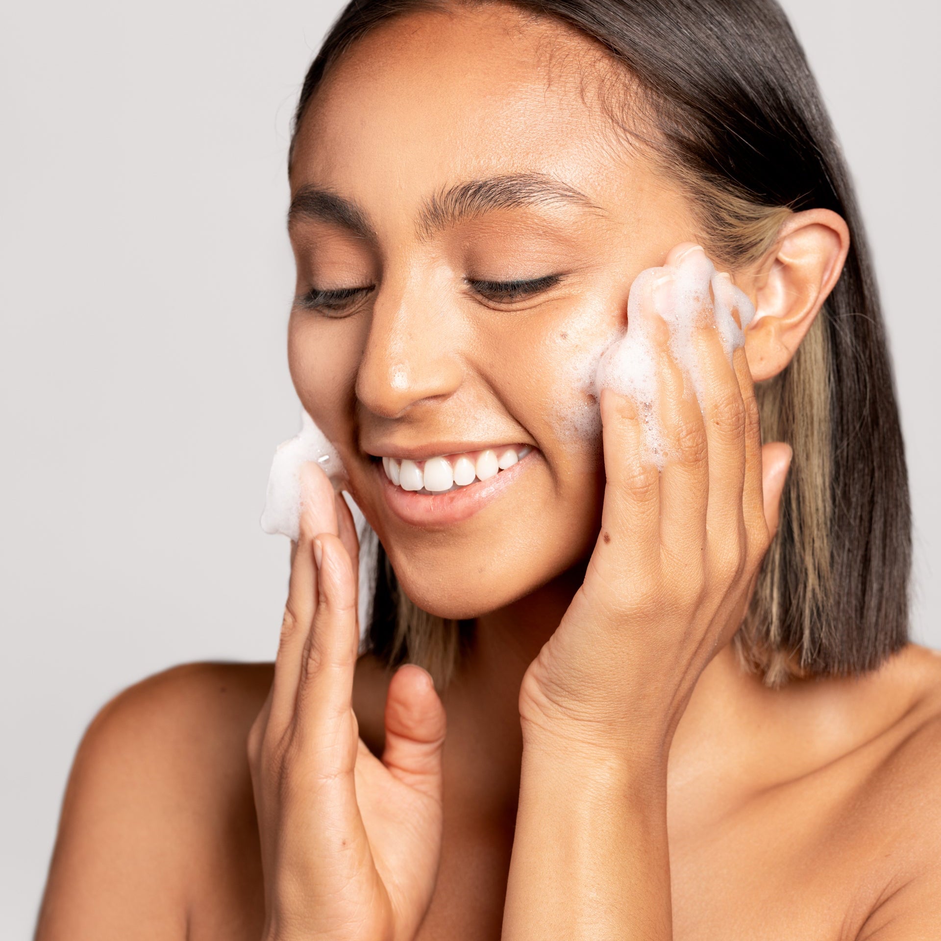 Woman applying cream to her face against a plain background