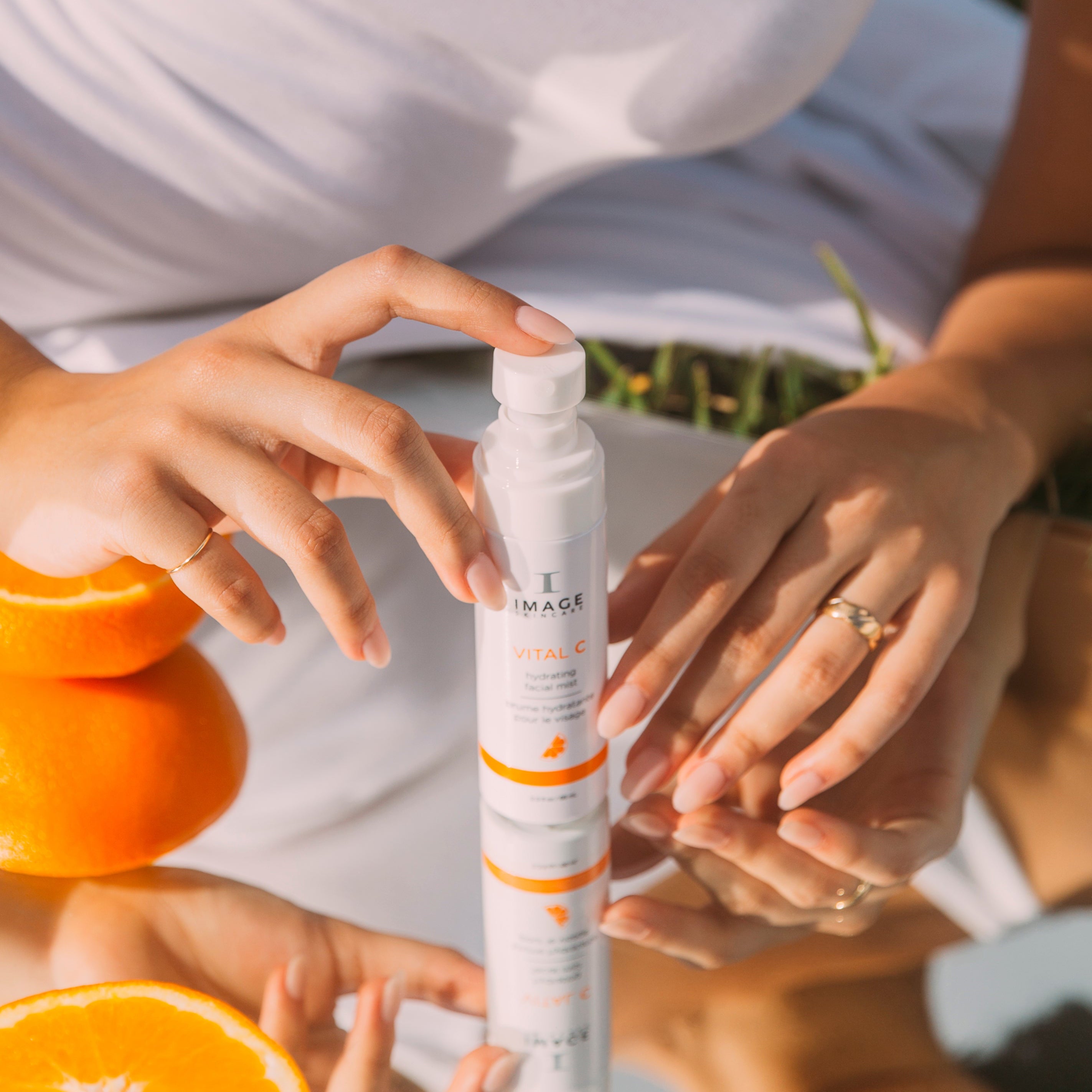 Person holding a skincare product with oranges in the background