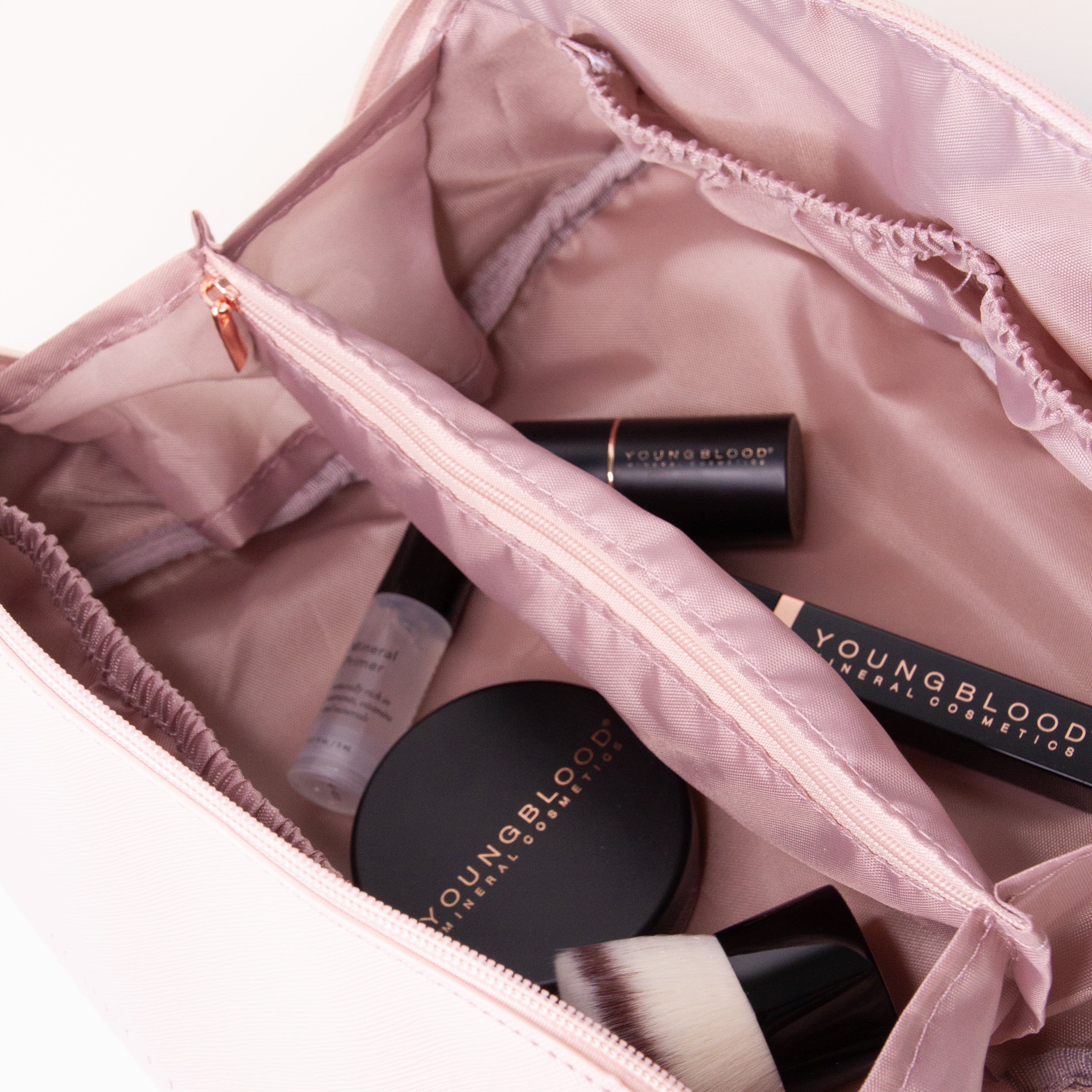 Open pink makeup bag with Youngblood products on a white background